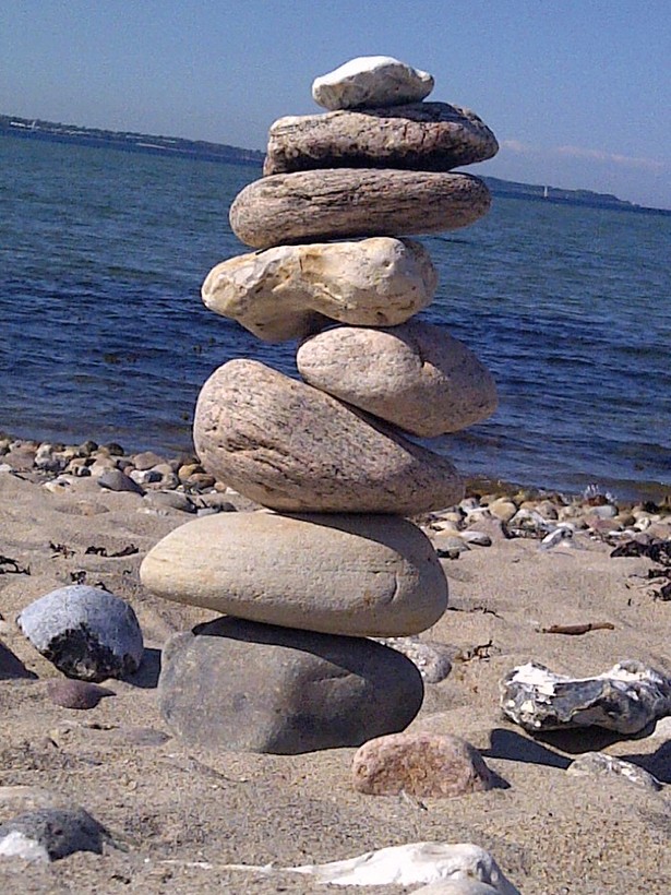 Mehrere Steine sind an einem Meeresstrand zu einem Turm aufeinandergelegt worden. Im Hintergrund ist das Meer zusehen.