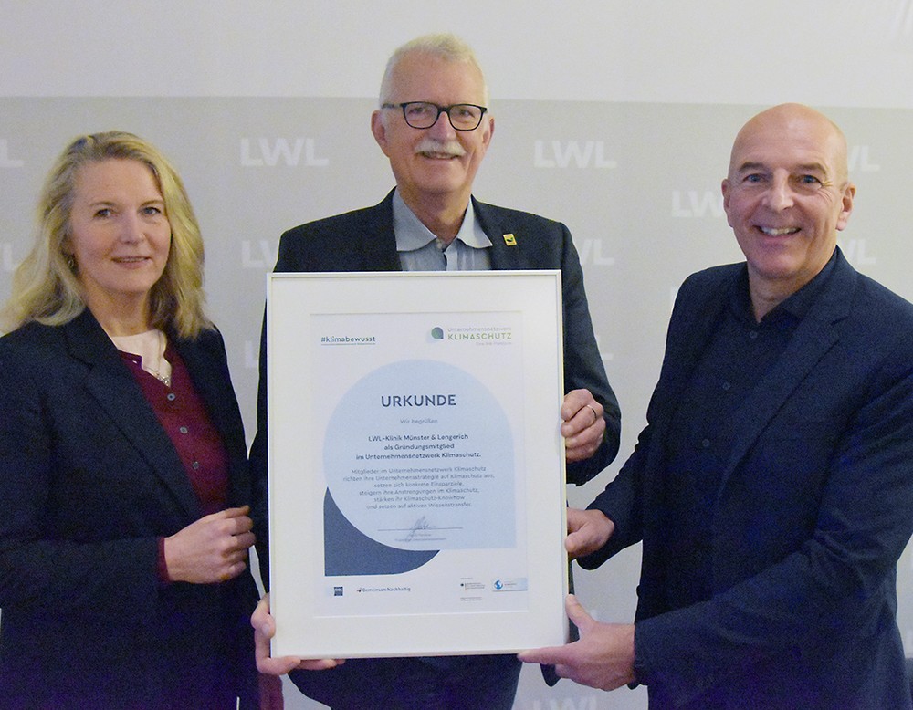 Drei Personen (zwei Männer und eine Frau) halten eine Urkunde