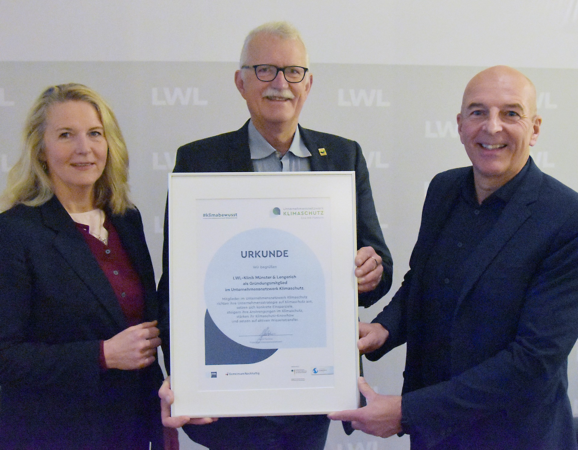 Drei Personen (zwei Männer und eine Frau) halten eine Urkunde
