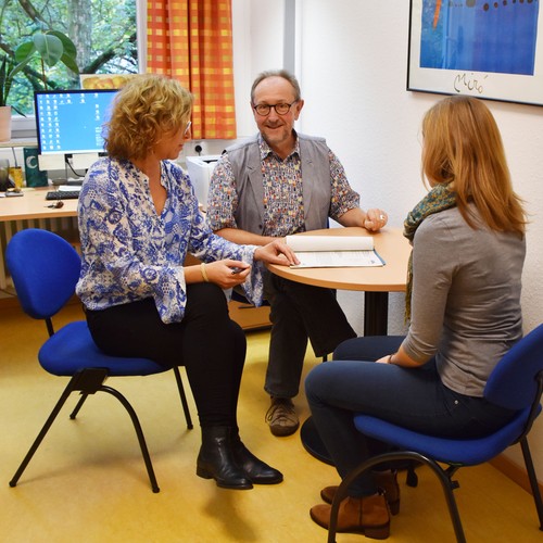 Zwei Frauen und ein Mann sitzen vor einem Schreibtisch und unterhalten sich