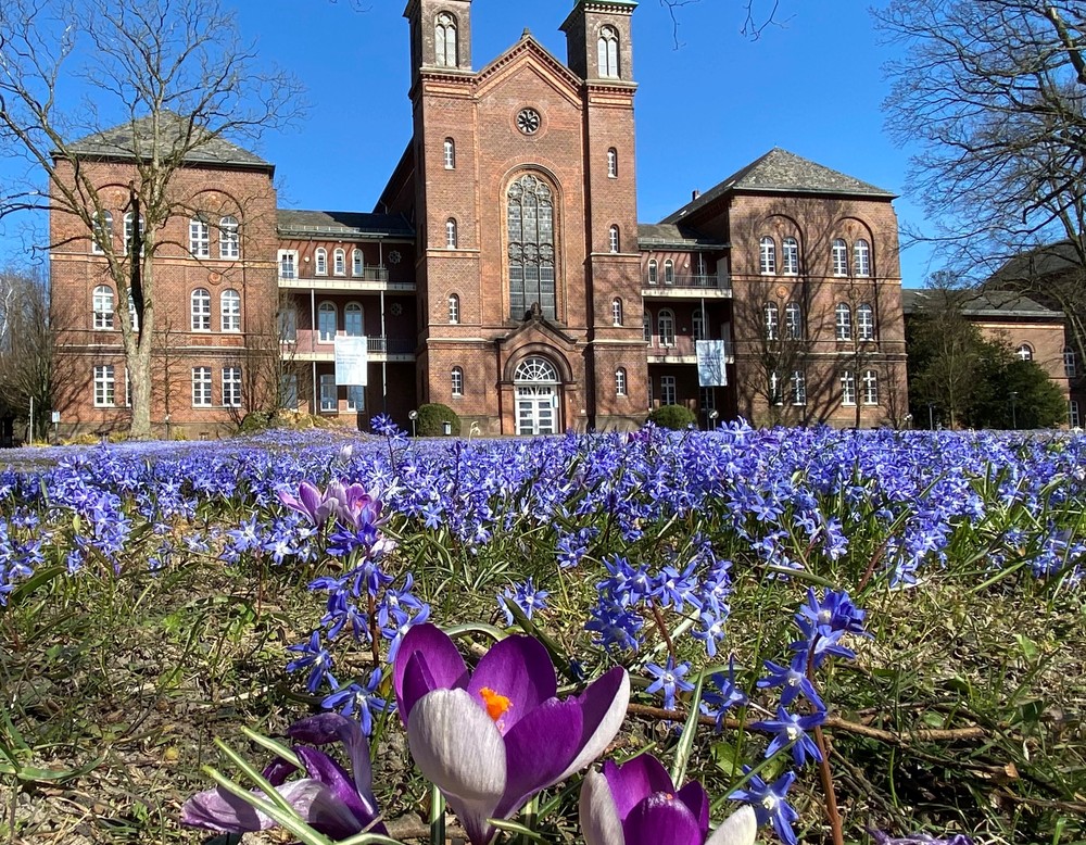 Titelfoto des Fortbildungsprogramms, Gebäude der LWL-Klinik Lengerich, im Vordergrund Wiese mit lila Blumen, Foto: Marita Unterauer
