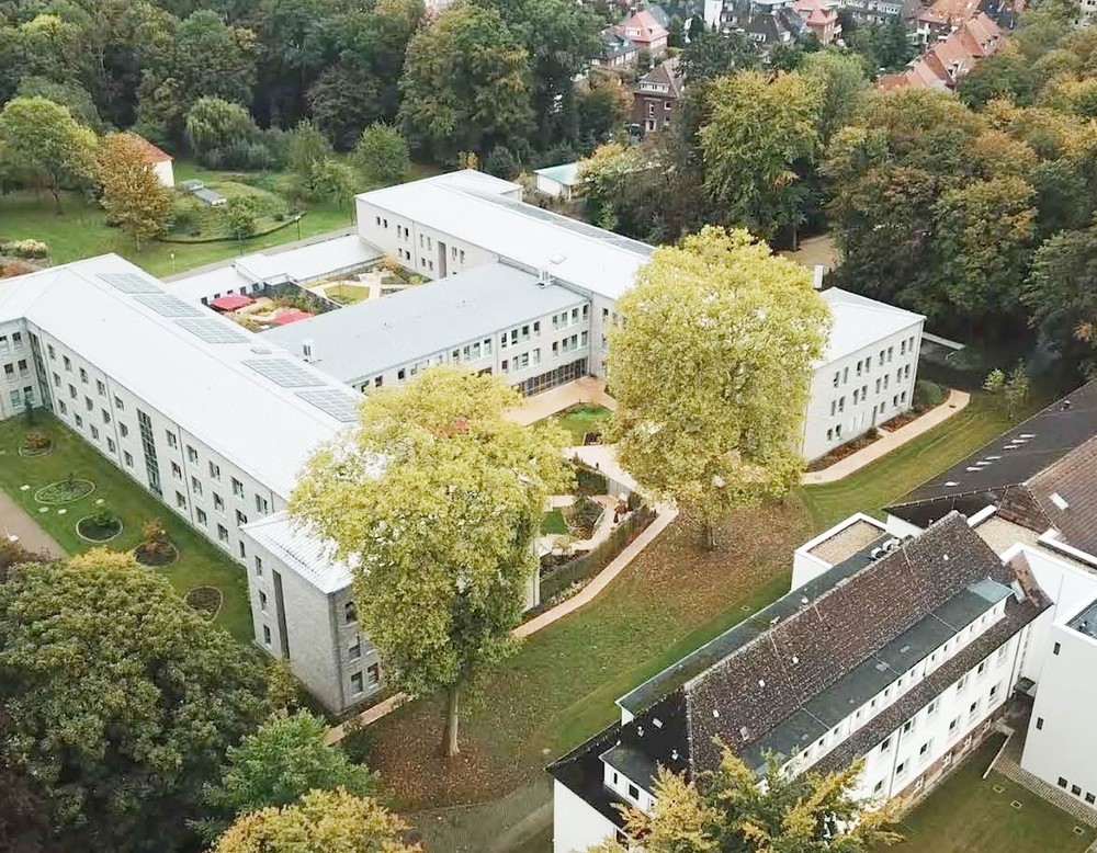 Luftbild auf das hellgraue, moderne Hauptgebäude der LWL-Klinik Münster, gelegen in dem großflächigen, grünen Klinikpark.