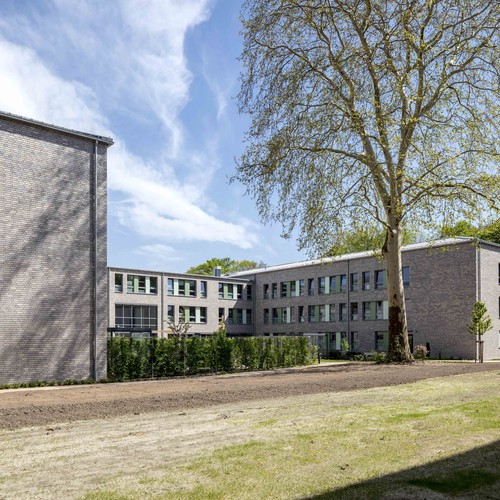 Modernes zweistöckiges, graues Gebäude, davor ein grüner Rasen