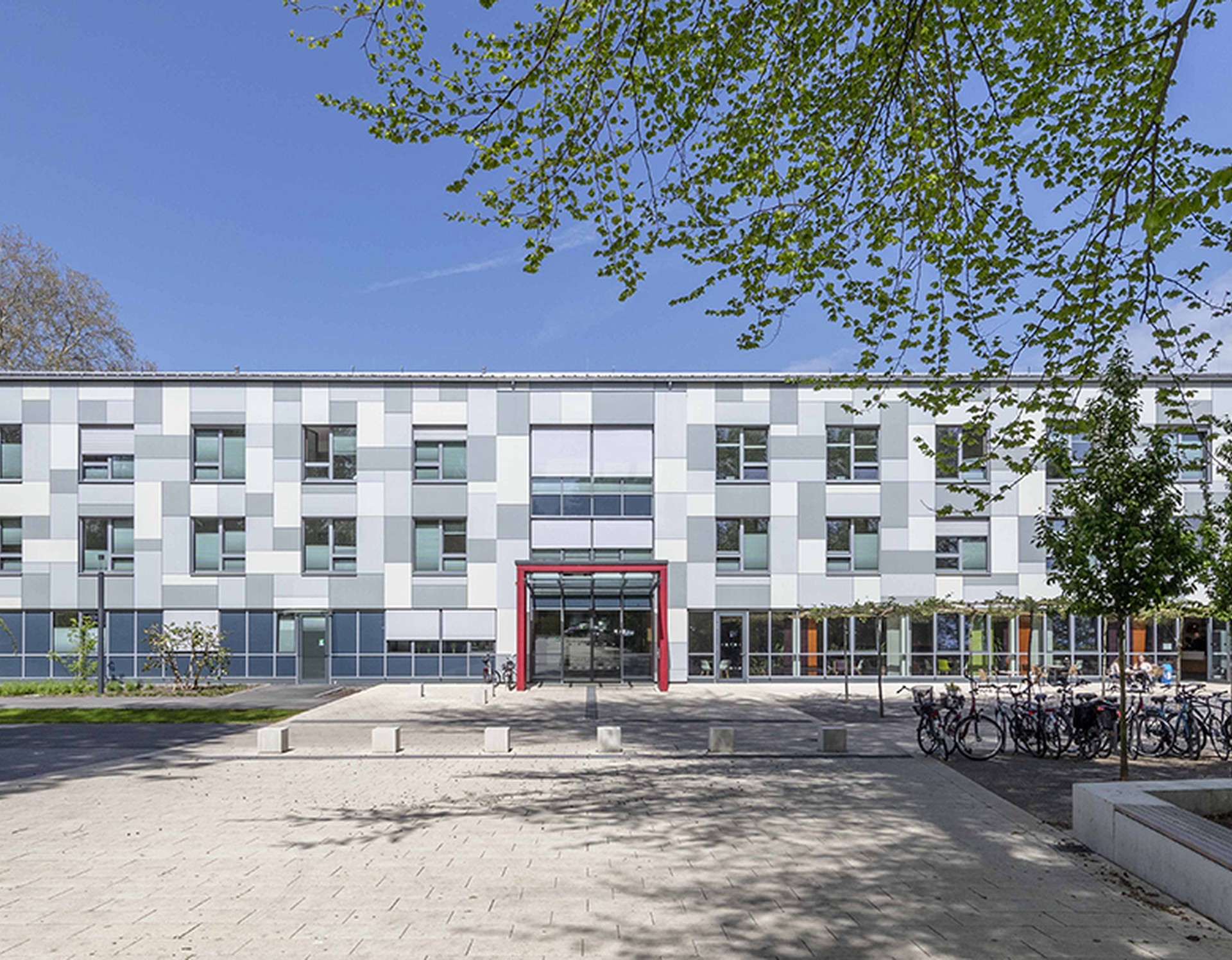 Das weiße, moderne Hauptgebäude der Klinik, roter Türrahmen im Eingangsbereich, viele Fahrräder vor dem Gebäude
