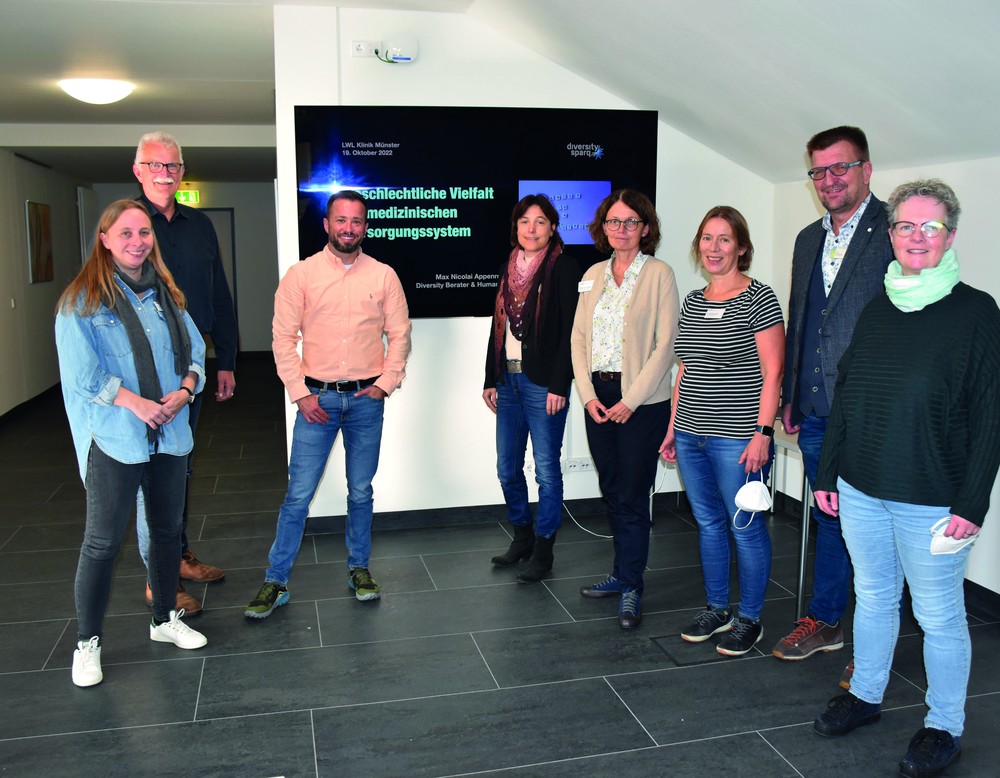 Titelfoto des Fortbildungsprogramms: Auf einer grünen Wiese stehen 150 Menschen, die das Friedenszeichen bilden.